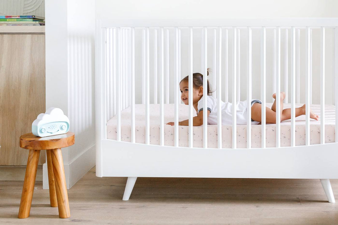 A baby lays in a crib listening to SNOObie white noise machine
