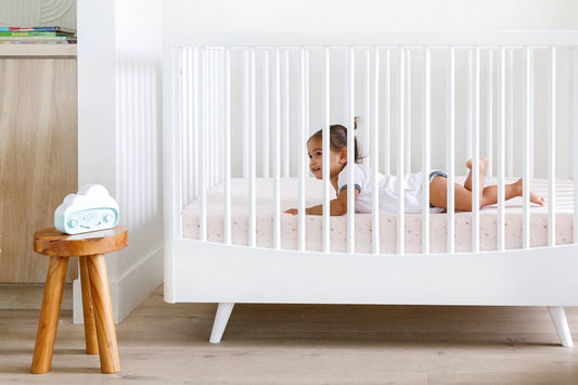 A baby lays in a crib listening to SNOObie white noise machine