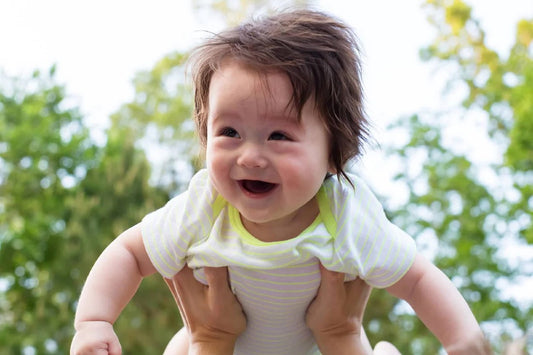 A smiling baby being lifted in the air outside