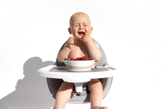 A baby eats a bowl of berries