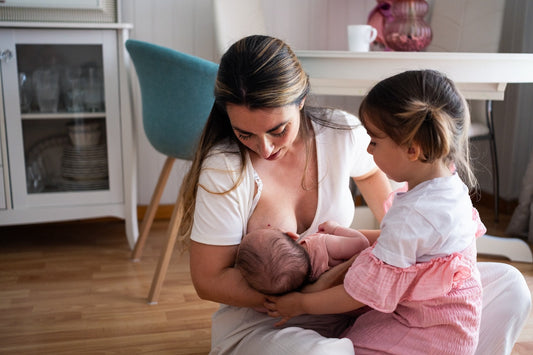 A mum nurses her newborn while her toddler sits nearby