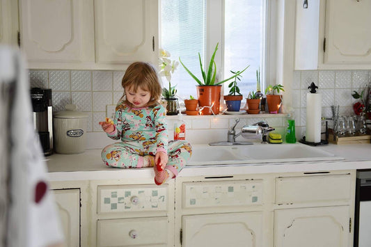 A toddler girl sits on the kitchen counter and eats a snack in her PJs